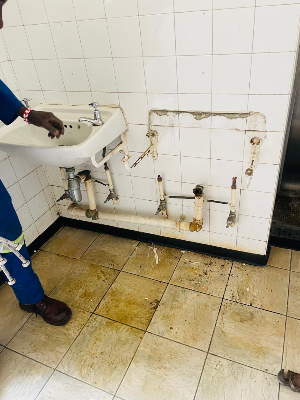 Worker inspecting exposed basin plumbing in a tiled washroom